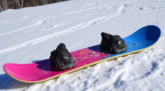 A beginner-friendly snowboard with soft bindings and boots next to it on a gentle snowy slope